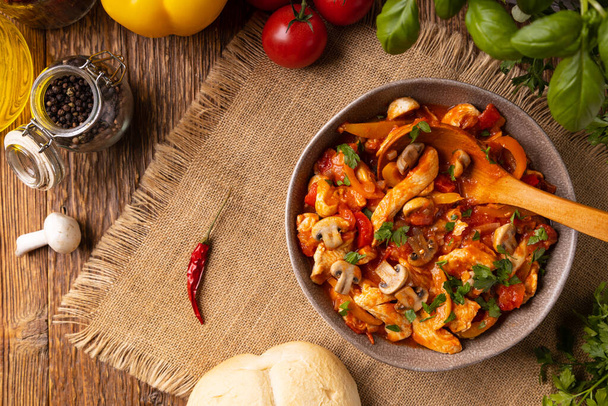 Chicken stew with peppers, mushrooms and tomatoes. Wooden background.  - Fotoğraf, Görsel