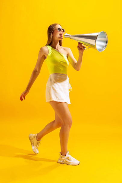 Attention sales. Excited young girl, student going with big retro megaphone isolated on bright yellow background. Concept of beauty, art, summer fashion, emotions and facial expressions. Copy space - Φωτογραφία, εικόνα