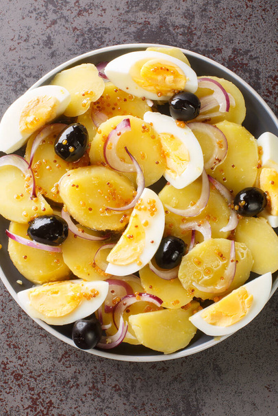 Oriental salad is a favorite of Romanians potato salad with onions, olives and boiled eggs close-up on a plate on the table. Vertical top view from abov - Zdjęcie, obraz