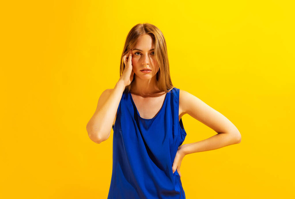 Terrible headache, pain. Young sad girl, student touching her head with hand isolated on bright yellow background. Concept of health, medicine, emotions and facial expressions - Photo, Image