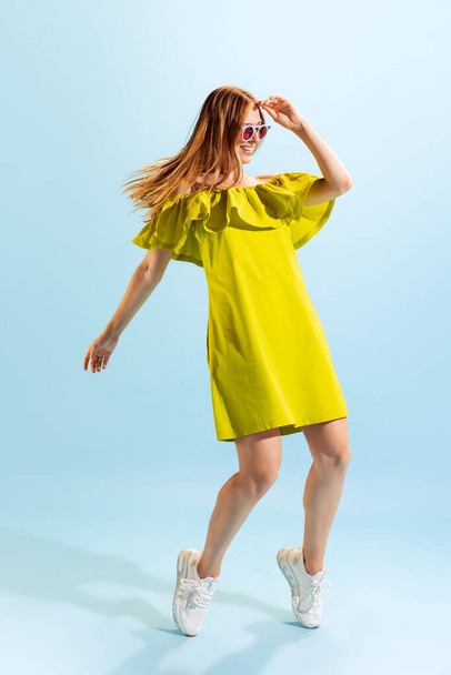 Fashion. Studio shot of young beautiful blonde in summer yellow dress isolated on light blue background. Concept of beauty, art, style, youth, healthy lifestyle. Copyspace for ads, text, sales offer. - Foto, afbeelding