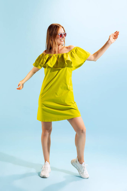 Enjoying summer life. Young beautiful blonde in summer yellow dress isolated on light blue background. Concept of beauty, art, fashion, youth, healthy lifestyle. Copyspace for ads, text, sales offer. - Photo, Image