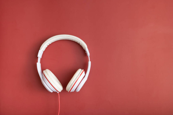 White-colored headphones on red background. Minimalistic fashion music concept. Copy space. Top view, flat lay. - Foto, imagen