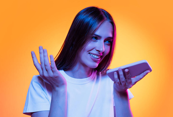 Half-length shot of emotional girl with long glossy dark hair isolated on orange background in neon light. Concept of beauty, art, fashion, youth, sales and ads. - 写真・画像