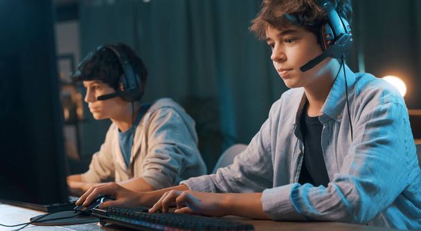 Young gamers wearing headsets and playing online multiplayer video games at home - Foto, Bild