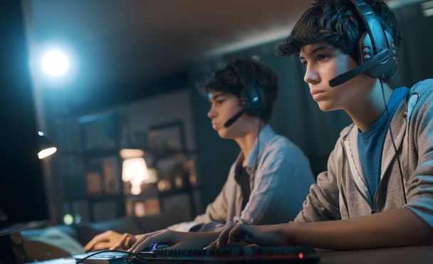 Teenager friends playing online video games together, they are wearing headsets and staring at the computer monitor - Foto, Imagem