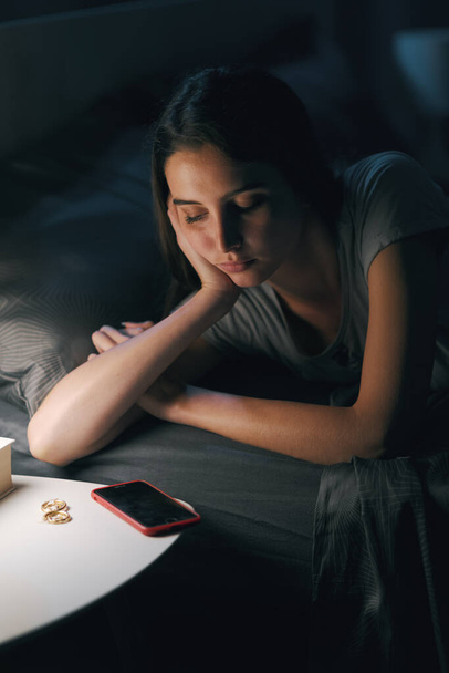Sad young woman lying in bed and suffering from insomnia, she is staring at her smartphone - Photo, Image