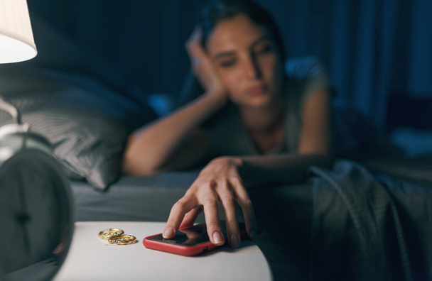 Sad young woman checking her phone at night, she has a smartphone addiction - Foto, imagen