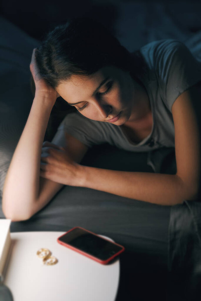 Sad young woman lying in bed and suffering from insomnia, she is staring at her smartphone - Photo, image