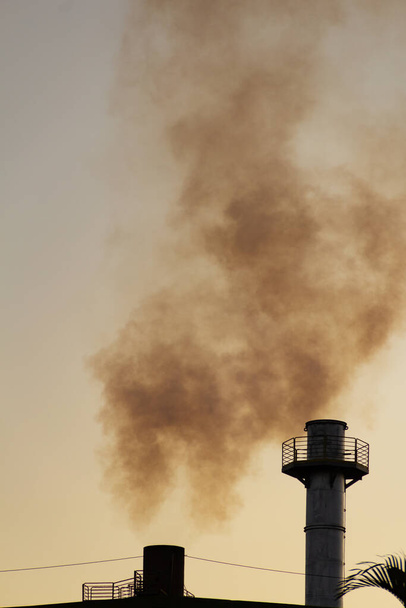 Smoke coming out of the factory chimney. Air pollution by smoke coming out of a factory chimney with the opaque sky in the background. - Foto, Bild