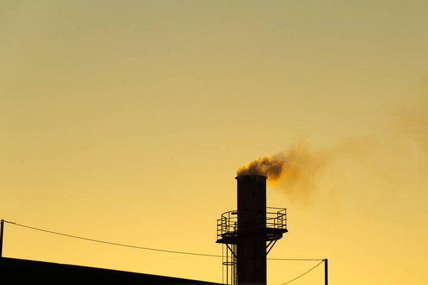 Smoke coming out of the factory chimney. Air pollution by smoke coming out of a factory chimney with the golden dawn sky. - Fotografie, Obrázek