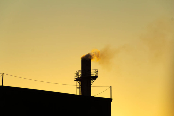 Smoke coming out of the factory chimney. Air pollution by smoke coming out of a factory chimney with the golden dawn sky. - 写真・画像