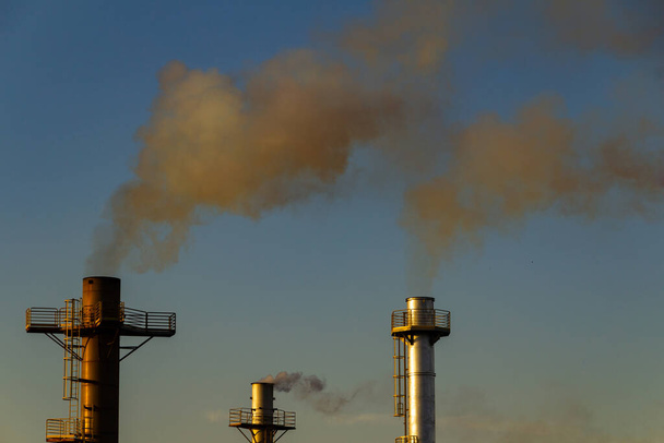 Дим виходить з заводських димоходів. Забруднення повітря від диму виходить з трьох димоходів заводу з блакитним небом на задньому плані
. - Фото, зображення