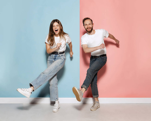 Fun, joy. Young stylish happy man and excited girl dancing hip-hop at studio on blue and pink trendy color background. Human emotions, youth, love and lifestyle concept - Fotografie, Obrázek
