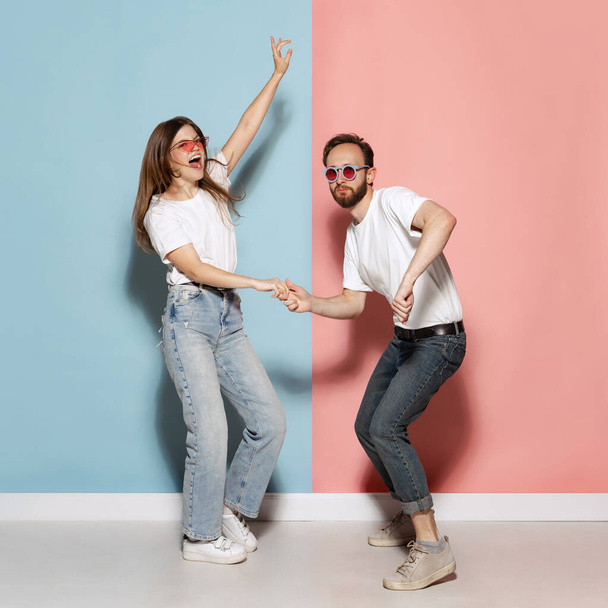 On style. Young stylish happy man and excited girl dancing hip-hop at studio on blue and pink trendy color background. Human emotions, youth, love and lifestyle concept - Foto, immagini