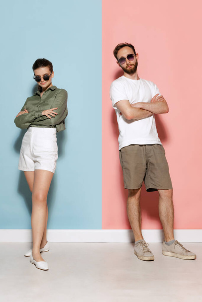 Relationship. Fashionable couple, handsome man and charming girl posing isolated over blue-pink background. Fashion, emotions, youth, love, travel, vacation concept - Valokuva, kuva
