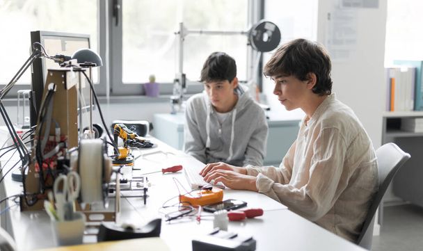 Students sitting at desk in the lab and learning 3D printing together, one is typing and the other is assisting him - Fotó, kép