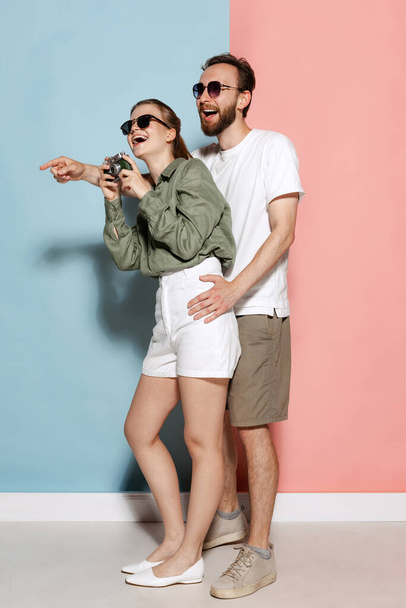 Vivid experience for family. Happy couple in love, handsome man and charming girl posing isolated over blue-pink background. Fashion, emotions, youth, love, travel, vacation concept - Photo, image
