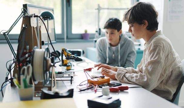Students sitting at desk in the lab and learning 3D printing together, one is typing and the other is assisting him - Фото, зображення