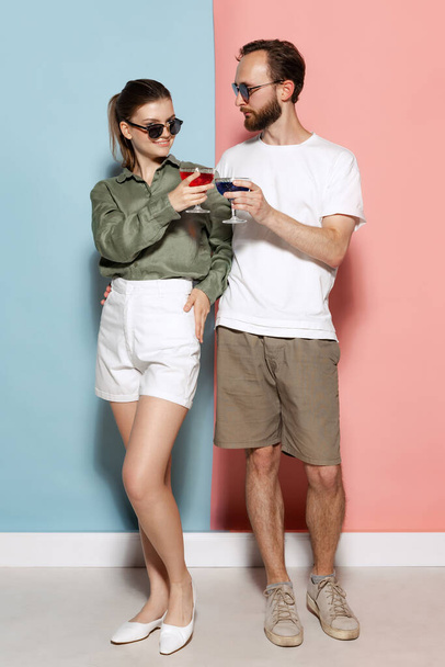 Dating, flirting. Fashionable couple, handsome man and charming girl posing isolated over blue-pink background. Fashion, emotions, youth, love, travel, vacation concept - Фото, изображение
