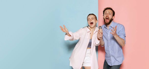 Karaoke. Couple of young funny and happy man and woman having fun isolated over blue and pink background. Human emotions, youth, love and active lifestyle concept - Foto, imagen