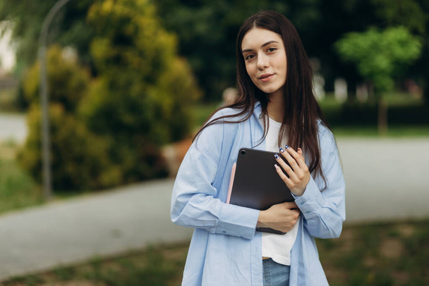 Portrait of an attractive student girl holding a gadget in her hands. The girl looks at the camera. Copy space - Foto, immagini