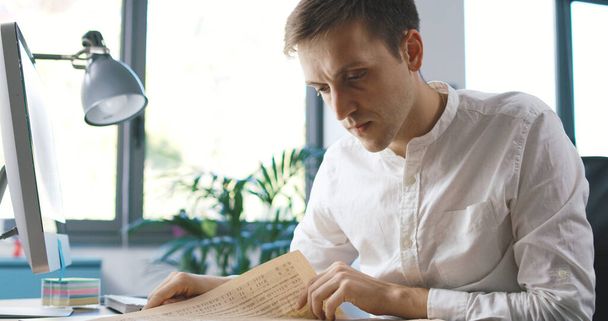 Man sitting at desk in the office and reading a newspaper, he is focused and thinking - Фото, изображение