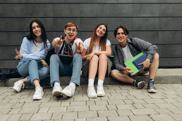 Group of happy smiling students sitting on the floor against dark wall. College learning concept - Φωτογραφία, εικόνα
