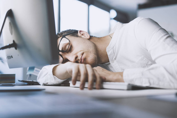 Lazy office worker sleeping at his desk, he is exhausted and stressed - 写真・画像