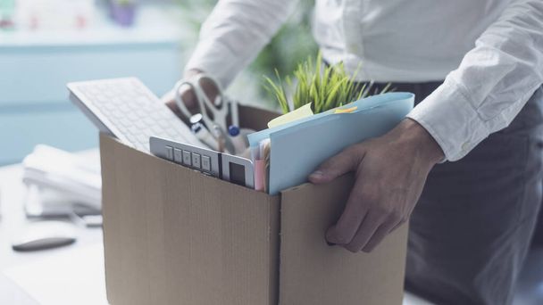 Fired office worker packing his belongings in a cardboard box and leaving the office, crisis and unemployment concept - 写真・画像