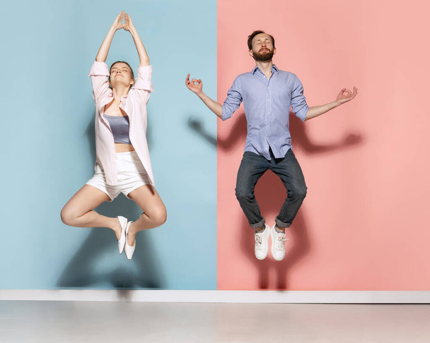 Meditation. Funny man and woman levitating isolated over blue and pink background. Human emotions, youth, love and active lifestyle concept. Couple having fun together - Zdjęcie, obraz