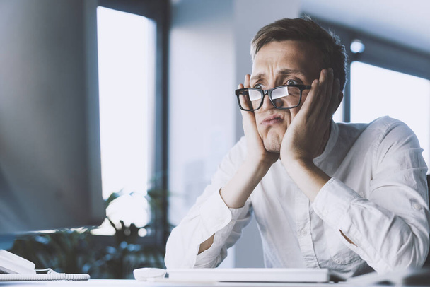Insane stressed office worker having a nervous breakdown, he is sitting at desk with head in hands, job burnout concept - Fotografie, Obrázek