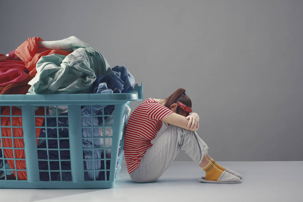 Tiny woman sitting next to a huge full laundry basket, household chores concept - Foto, Bild
