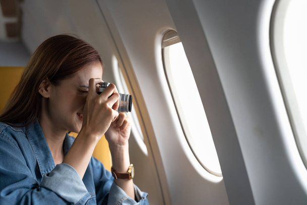 Beautiful Asian woman take a photo with camera in airplane. - Zdjęcie, obraz