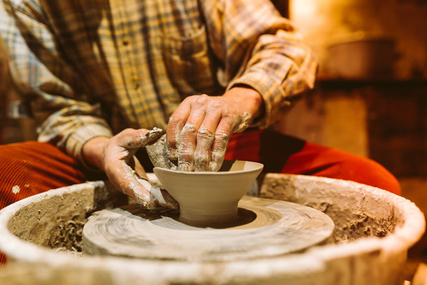 pottery in workshop of ceramist. potter's hands working with clay on potter's wheel, forming bowl. Traditional pottery, craft handicrafts, authentic atmosphere - Foto, afbeelding