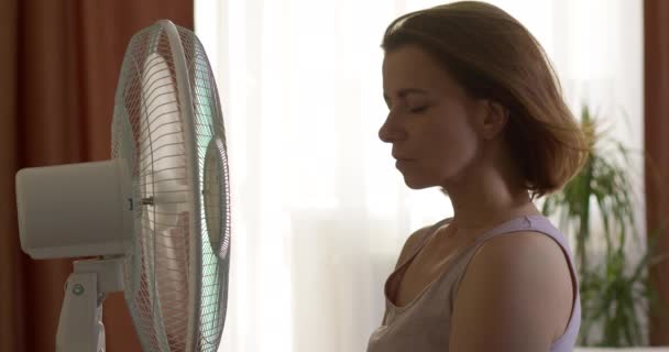 A woman is cooled by an electric fan in the heat in the room. - Záběry, video