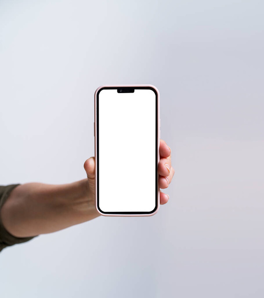 Hand of mature woman holding smartphone with white screen isolated on white background. Modern phone with touch screen in woman hand. Close up. Mock up mobile app advertising. No face visible. - Foto, Bild
