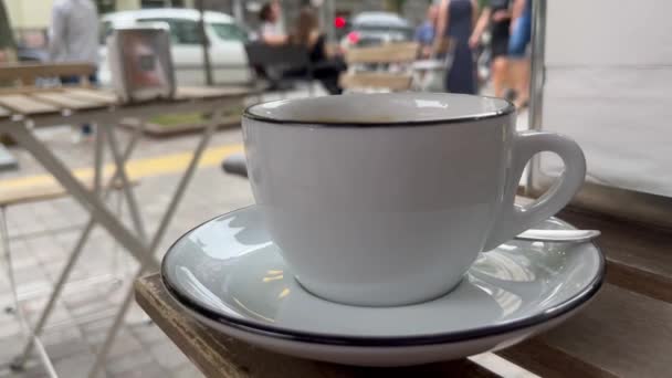 Street cafe with cup of fresh coffee or tea on a table. People are going on background. Summer city concept. High quality 4k footage - Video