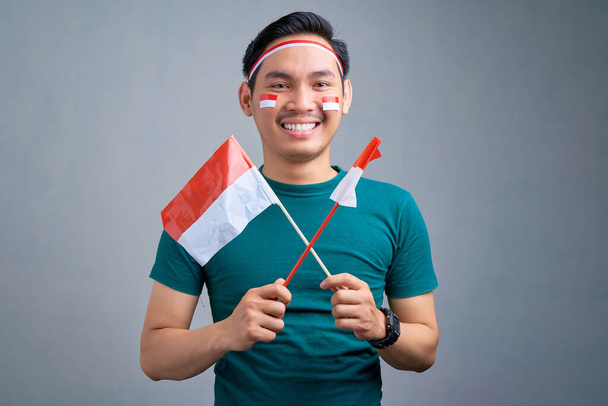 Portrait of cheerful young Asian man holding indonesian flag isolated on grey background. indonesian independence day on 17 august concept - Photo, image