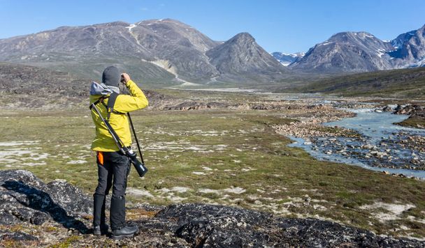 Male lookout armed with rifle scanning for polar bears in the tundra at Camp Frieda on the Disko Bay coast, Greenland on 18 July 2022 - Фото, изображение