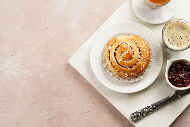 A round cinnamon pastry on a white plate on marble board on light pink background, cup of coffee, jam, milk - Foto, Imagem
