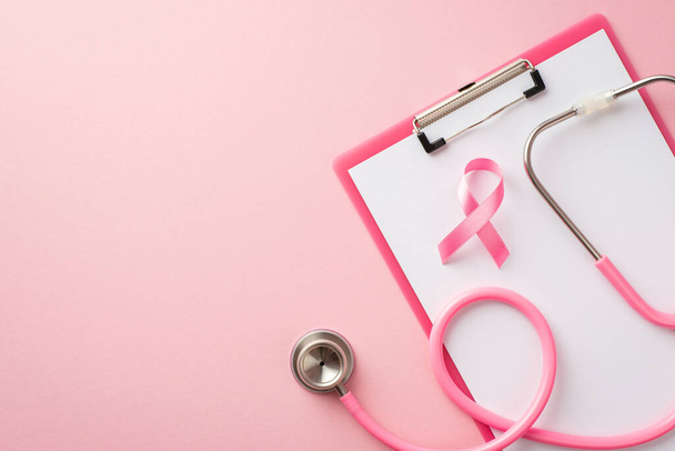 Top view photo of pink ribbon symbol of breast cancer awareness on clipboard and stethoscope on isolated pastel pink background - Fotografie, Obrázek