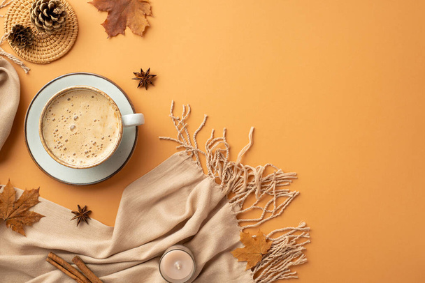 Autumn concept. Top view photo of cup of coffee on saucer cinnamon sticks candle anise yellow maple leaves scarf rattan serving mat and pine cones on isolated orange background - Foto, imagen