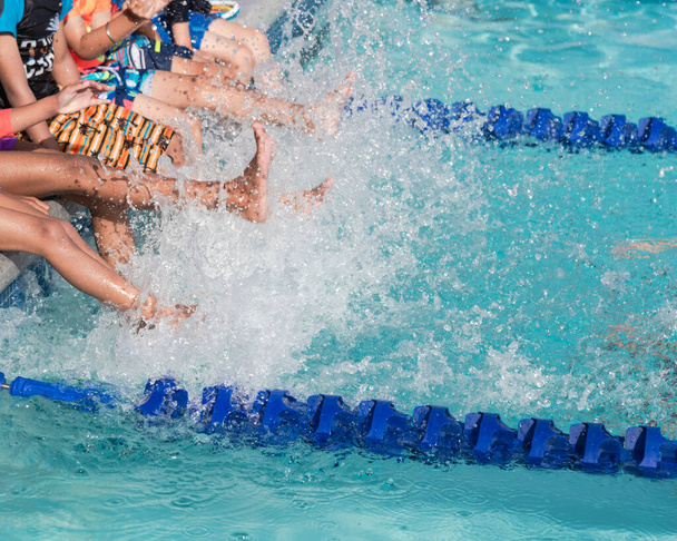 Grupa różnorodnych wielonarodowych dzieci kopiących rozpryskującą wodę na basenie klasy pływackiej w północnym Teksasie, w Ameryce. Dzieci w strojach kąpielowych w klasie basenu uczą się pływać - Zdjęcie, obraz