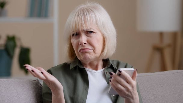 Frustrated senior lady Caucasian elderly woman with phone reads bad news in mobile message feel sad upset shock failure with smartphone app. Worried mature female user customer lost in online website - 写真・画像