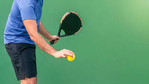 One caucasian man playing a match in the open with black padel racket and yellow ball at court outdoors. Paddle is a racquet game. Professional sport concept - Fotó, kép