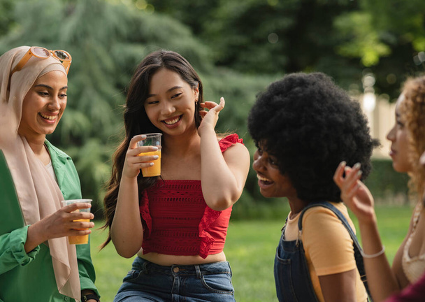 multiracial female friends having drink in park - focus on asian woman - - Foto, Bild