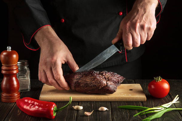 Professional chef slicing beef steak with knife on wood cutting board. Food preparation process concept - Foto, Imagem