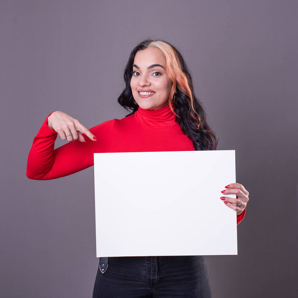 Beautiful woman pointing at a blank whiteboard against a grey background - Fotoğraf, Görsel