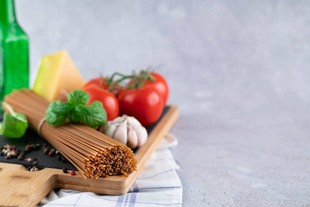 On a gray background, a blurred image of whole grain spaghetti, peppers, basil, tomatoes, cheese on a wooden board.Background with space for writing prescription text. - Photo, image